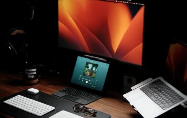 a wooden desk topped with a laptop computer next to a monitor