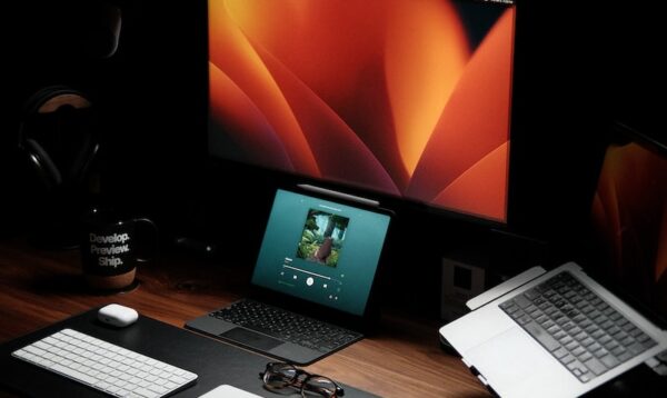 a wooden desk topped with a laptop computer next to a monitor